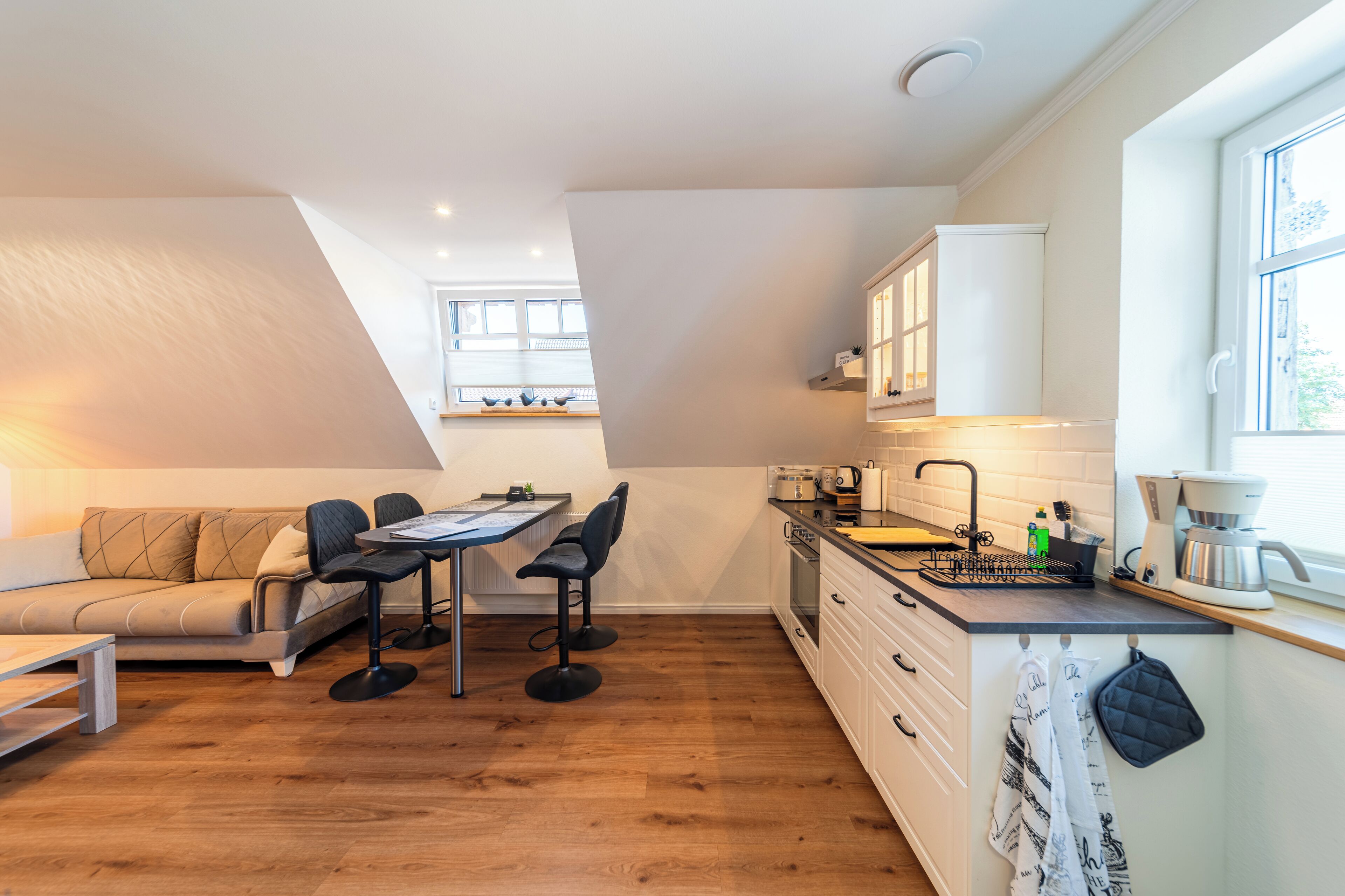 A compact kitchen with a dining area, wooden flooring, and a window providing natural light.