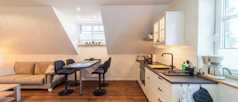 A compact kitchen with a dining area, wooden flooring, and a window providing natural light.