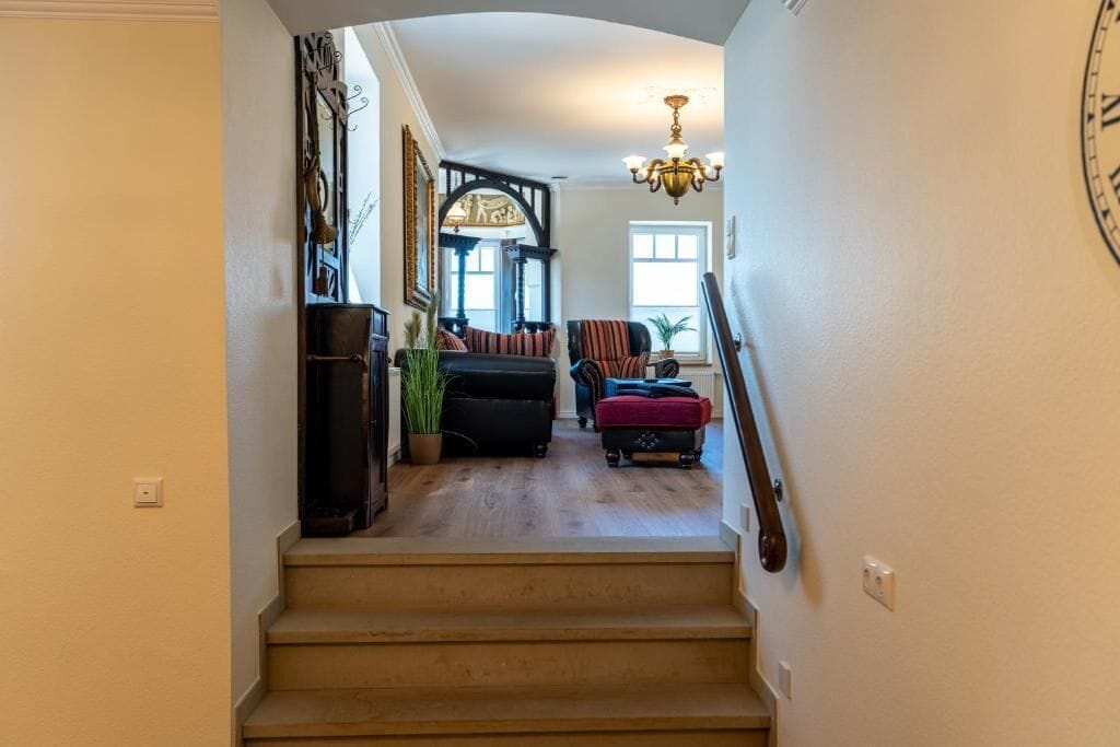 A staircase leading to a living room with a chandelier, a clock, and a view of the outside.