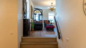 A staircase leading to a living room with a chandelier, a clock, and a view of the outside.