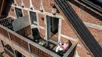 A balcony with a glass table and chairs, a brick building, and a wooden railing.
