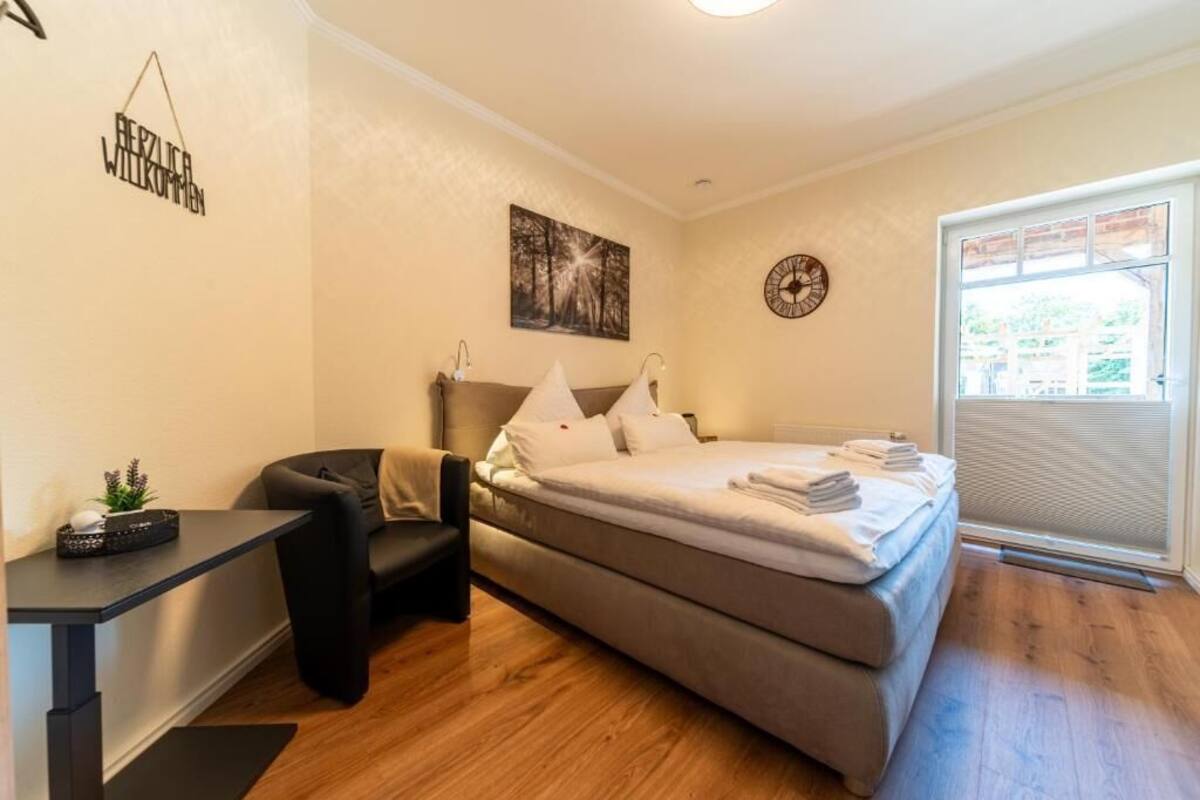 A bedroom with a bed, a desk, a chair, a wall clock, and a window.
