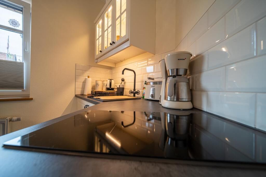Ett modernt kök med en svart bänkskiva, vita kakelplattor, en kaffebryggare och ett fönster med persienner.