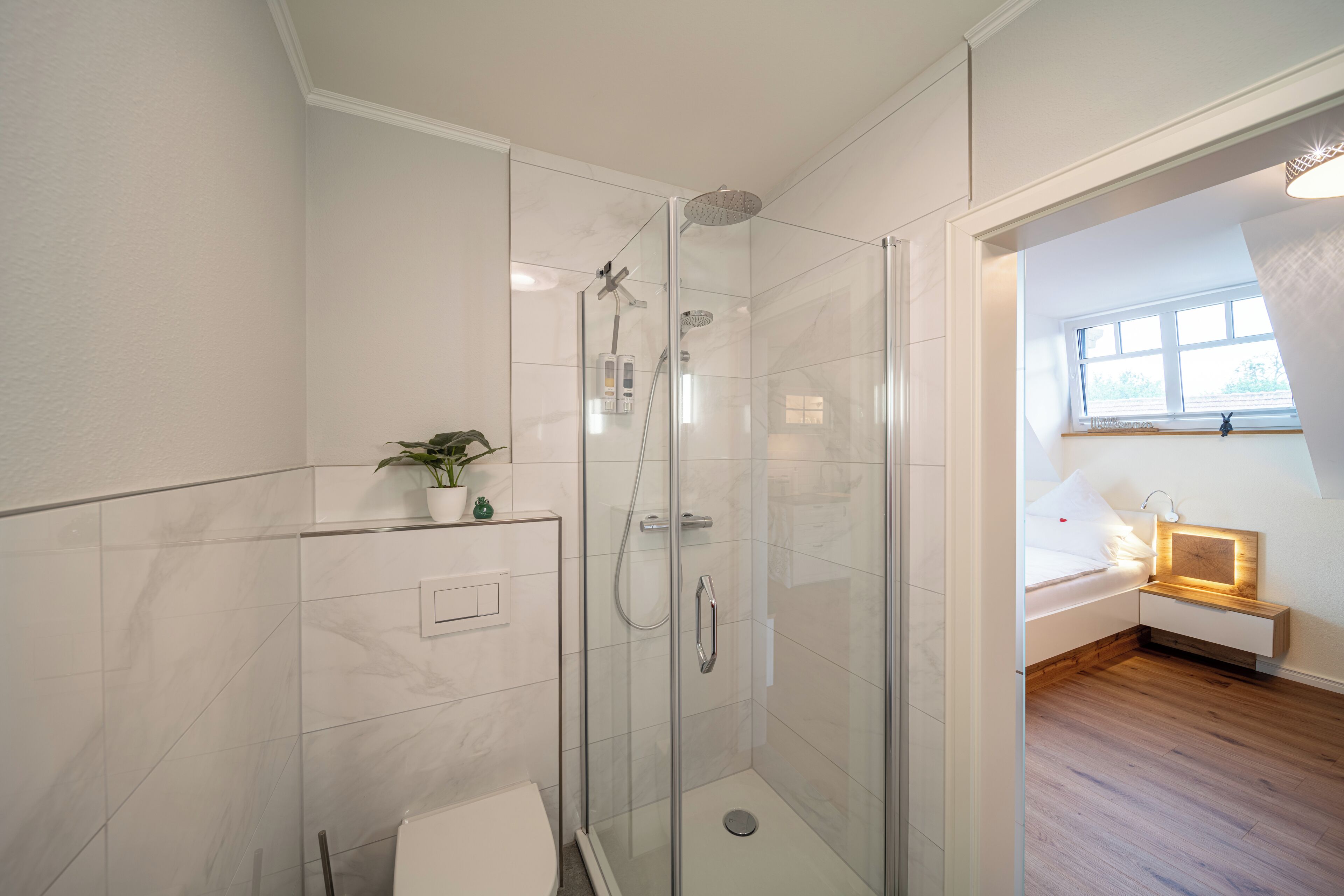 Un baño moderno con ducha envuelta en vidrio, inodoro y una pequeña planta en maceta.