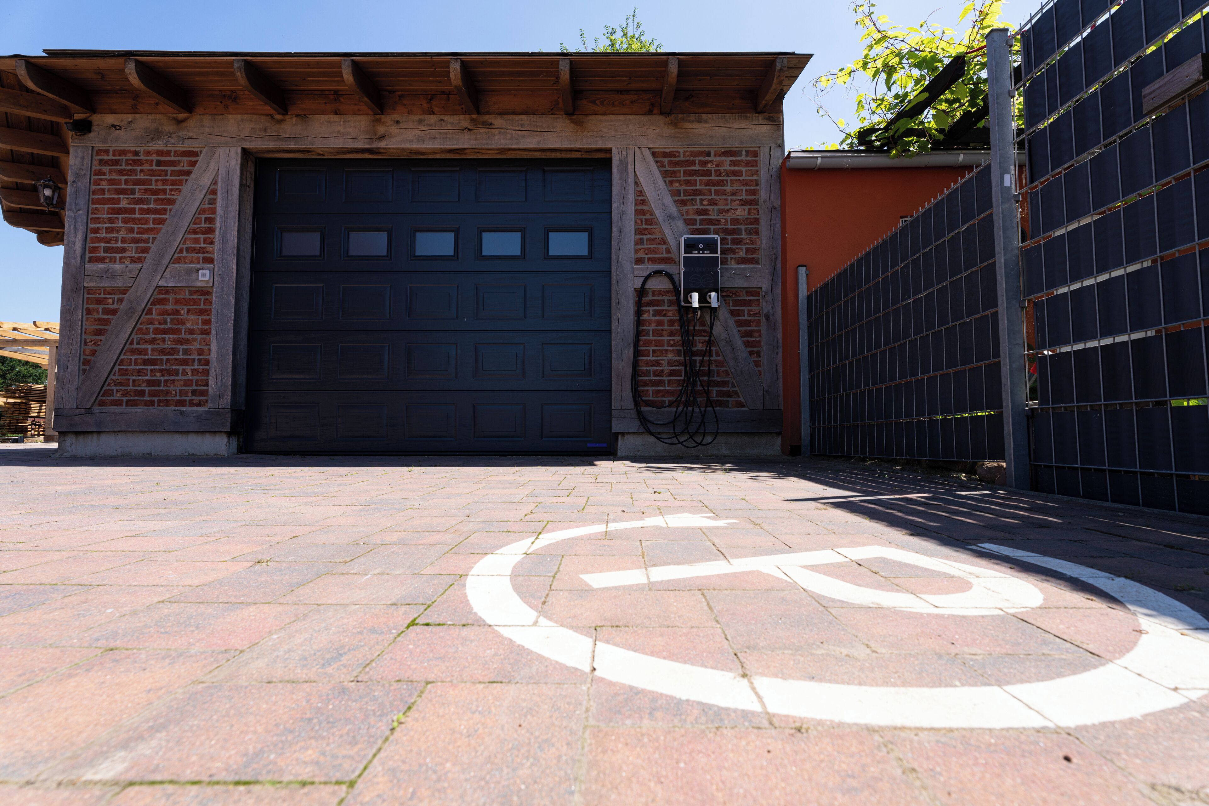 Edifici amb una porta garatge gran, façana de maó i zona d'entrada asfaltada amb el símbol de plaça d'aparcament per a persones amb mobilitat reduïda.