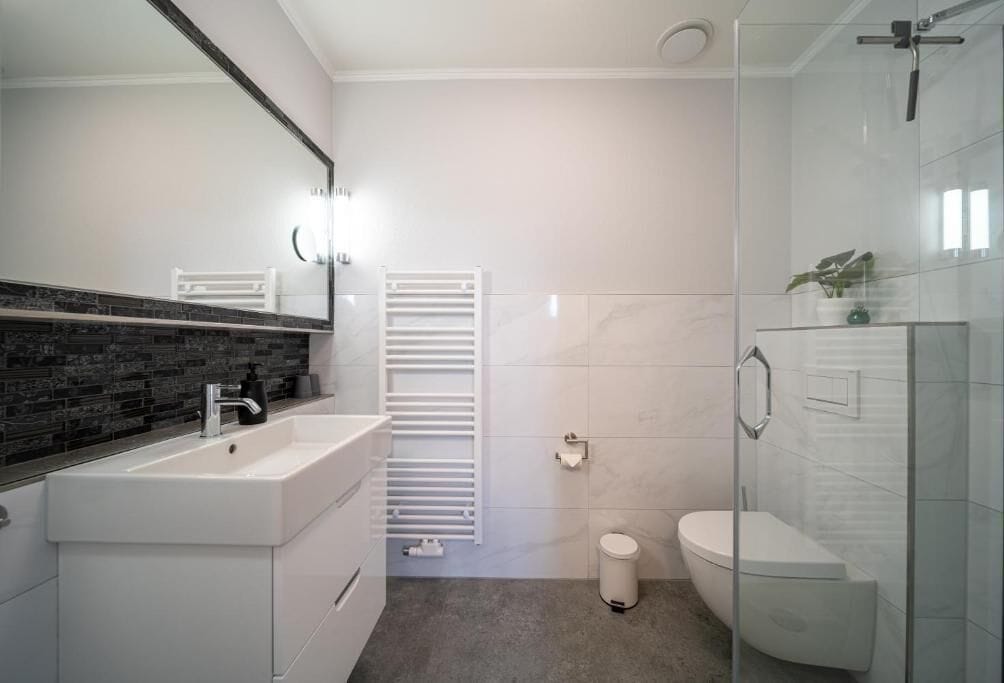 Een moderne badkamer met een witte wastafel, spiegel en toilet.