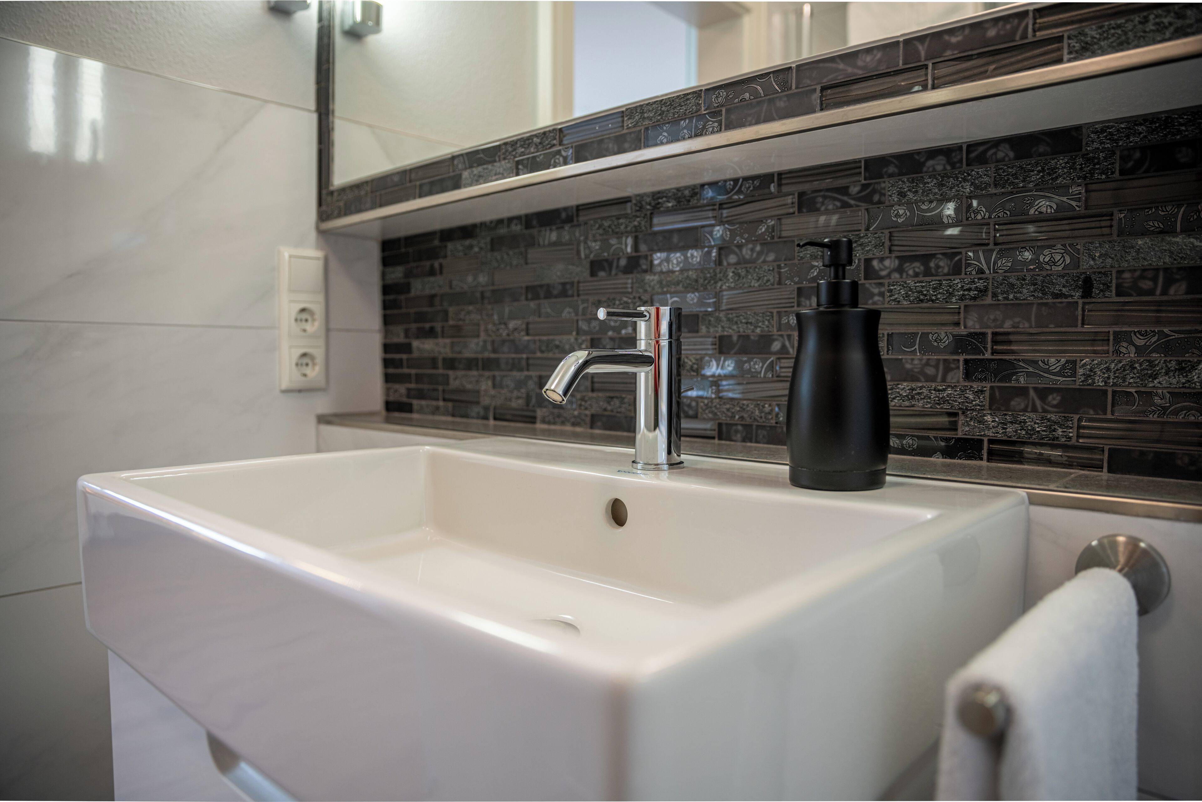 A bathroom with a white sink, a modern faucet, and a decorative tile backsplash.