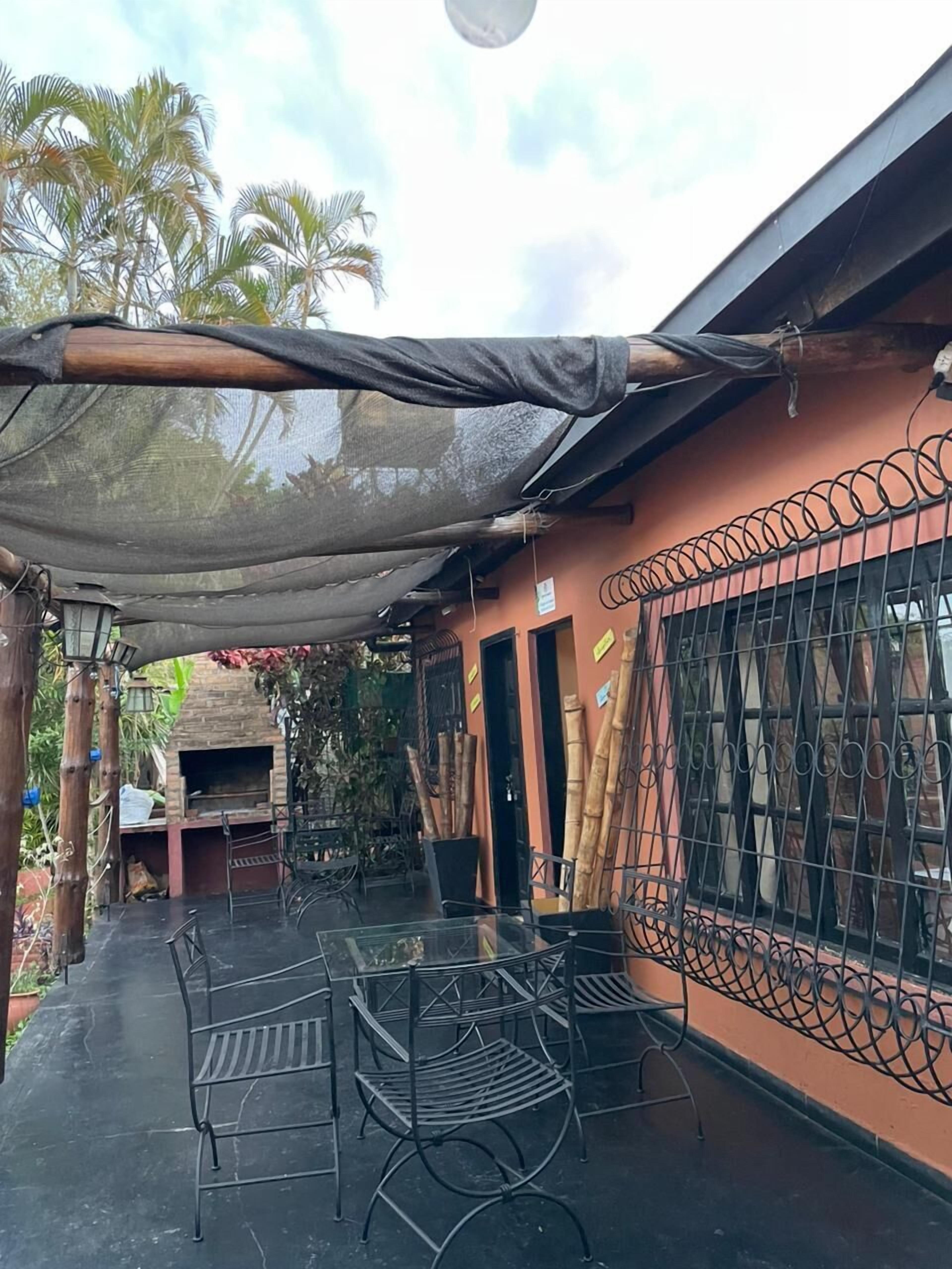 An outdoor patio with metal chairs and tables, a brick oven, and a covered area with a mesh canopy.