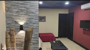 Una habitación con una cama roja, una mesa negra, un televisor de pared y un panel decorativo.