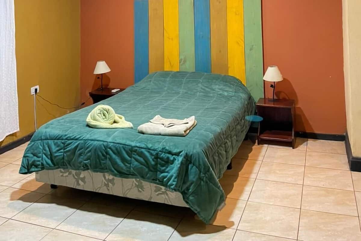 Une chambre à coucher avec un lit, deux tables de chevet avec des lampes, un appareil de climatisation et un mur rayé aux couleurs vives derrière le lit.