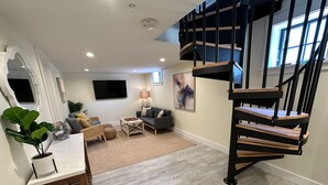 A modern living room with a wooden coffee table, a grey sofa, and a black staircase.