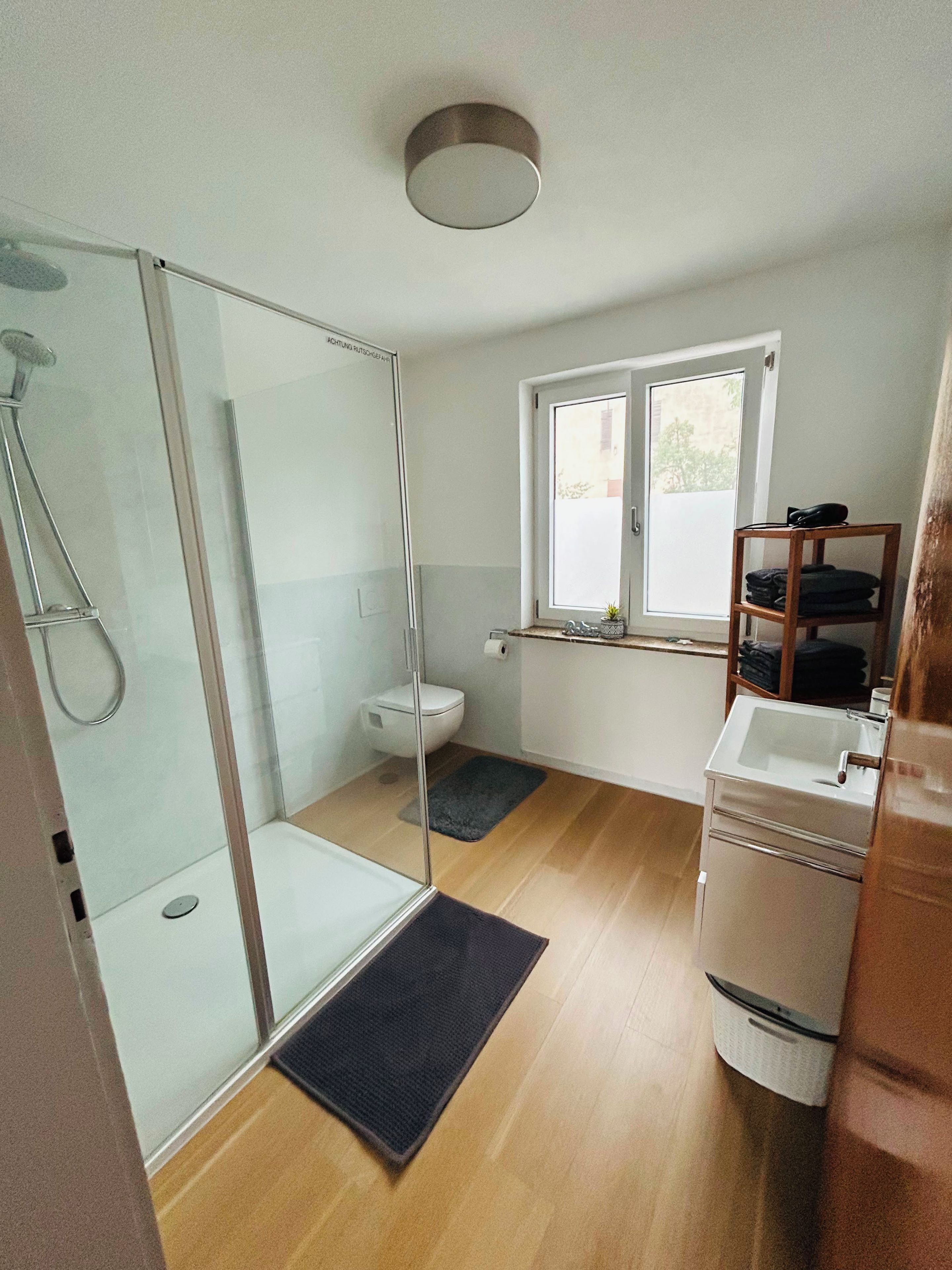 A modern bathroom with a glass shower enclosure, a toilet, a sink, and a window providing natural light.
