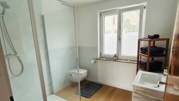 A modern bathroom with a glass shower enclosure, a toilet, a sink, and a window providing natural light.
