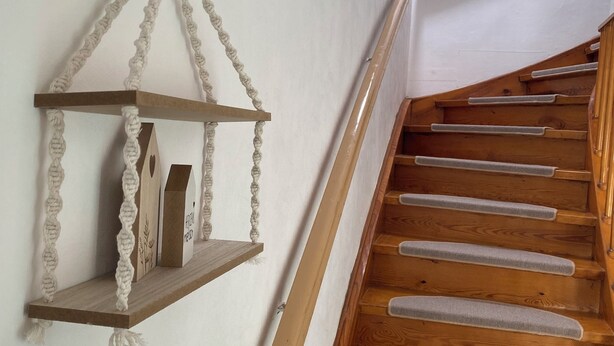 A wooden staircase with a handrail and a wall-mounted shelf with a macrame decoration. - Vacation apartment on the Danube cycle path (Untermarchtal)