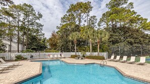 A rectangular swimming pool with clear blue water, surrounded by a white fence and shaded by tall trees.