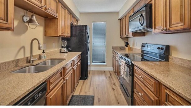 A compact kitchen with wooden cabinets, a stainless steel sink, a black refrigerator, a microwave, and a stove.