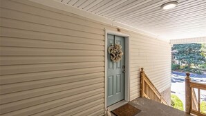 A covered porch with a light blue door, a wooden railing, and a small dog at the entrance.