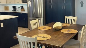 A kitchen with dark blue cabinets, a stainless steel refrigerator, a wooden dining table with placemats, and white chairs. - Beach/Marina/Walking trails and more… (Carrabelle)