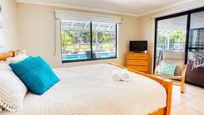Habitación de hotel con cama, televisión, cómoda de madera y balcón con mobiliario exterior.