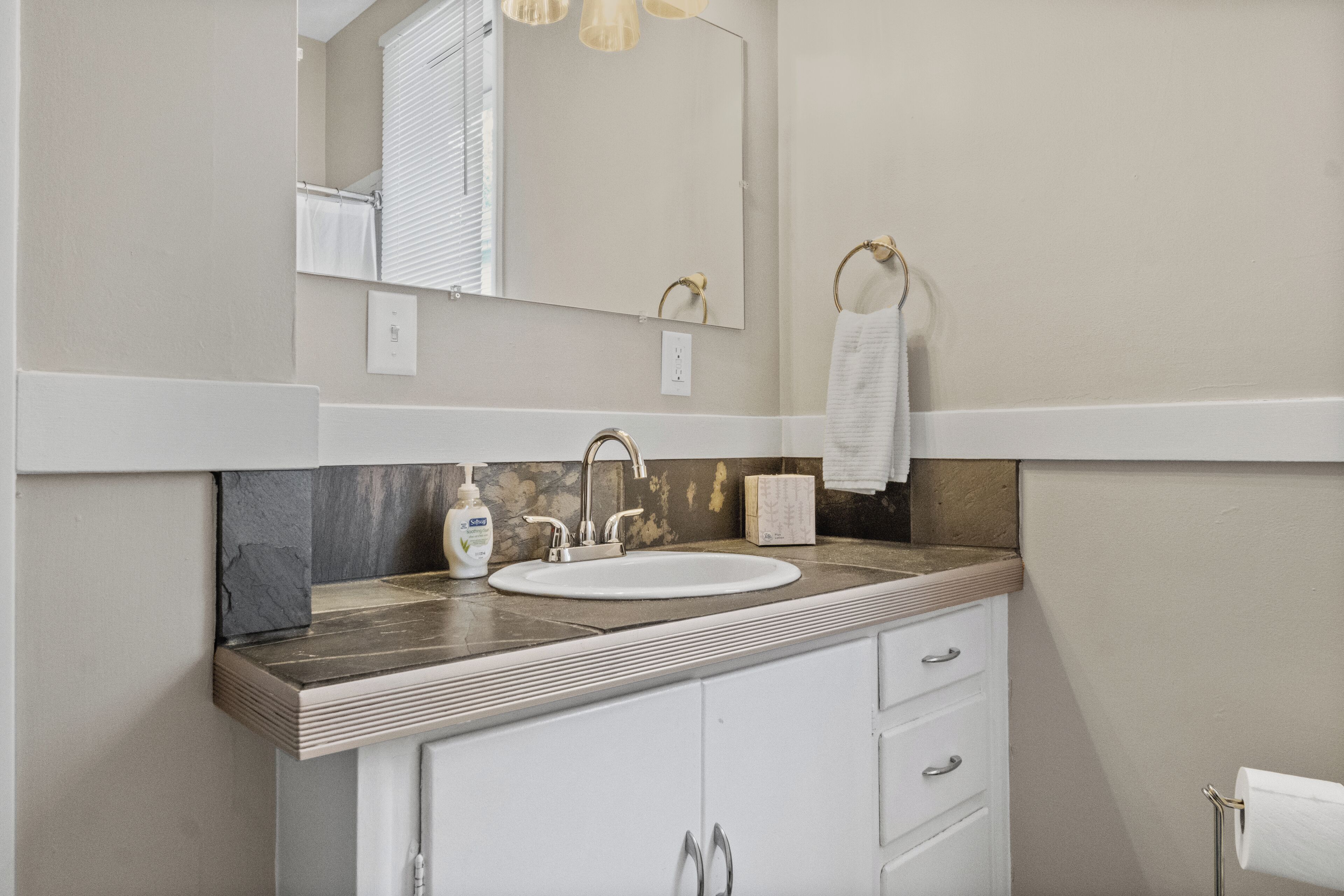 A bathroom with a white sink, a mirror, a towel rack, and a soap dispenser.