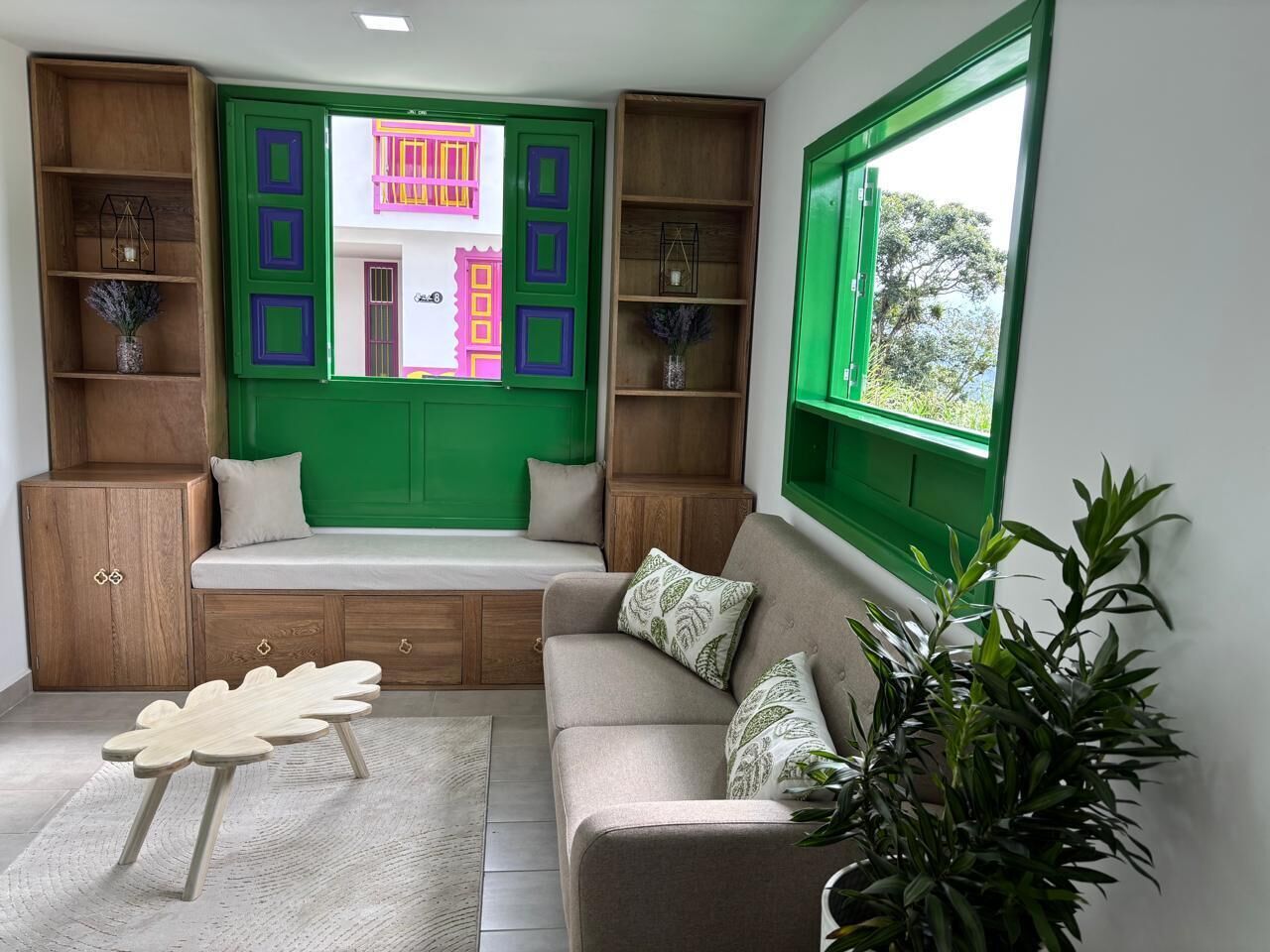 A cozy living room with a built-in bench, wooden shelves, and a large window with a view of greenery.