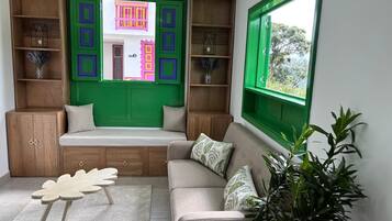 A cozy living room with a built-in bench, wooden shelves, and a large window with a view of greenery.