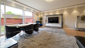 A modern living room with a large TV, a fireplace, and a dining area with a table and chairs.