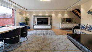 A modern living room with a large TV, a dining area with a table and chairs, and a sofa.