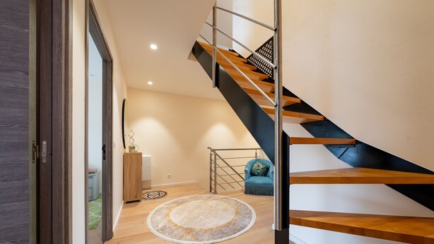 A modern interior with a wooden staircase, a round rug, and a blue chair.