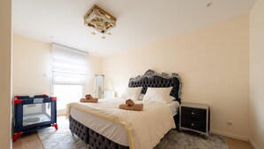 A bedroom with a large bed, a crib, a nightstand, and a chandelier.