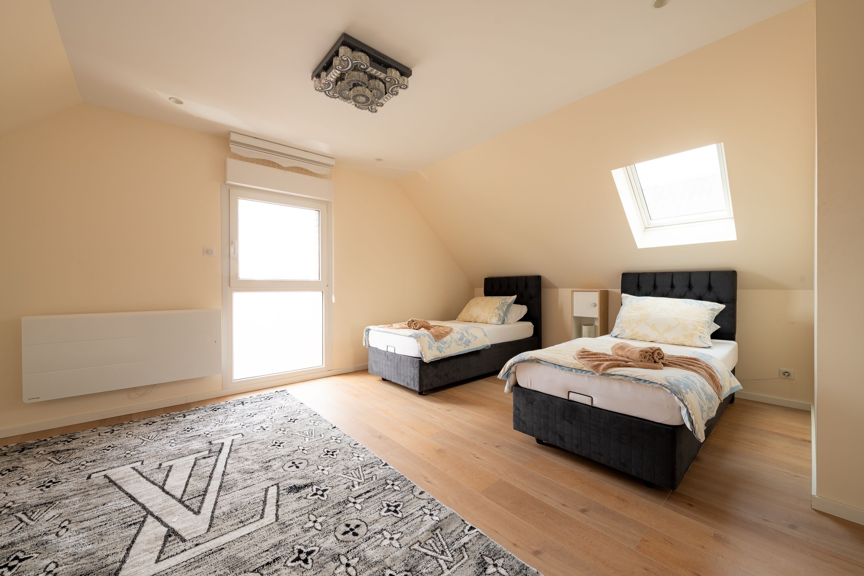 Een slaapkamer met twee bedden, een dakraam, een radiator en een kamerbreed tapijt met dessin.