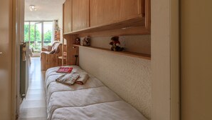 A narrow hallway with a bed, wooden shelves, and a view of an outdoor area.