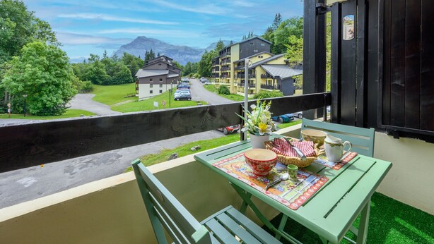 A balcony with a table set for breakfast, overlooking a road and buildings with a mountain in the background.
