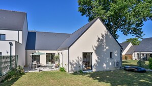 Una casa moderna con un amplio jardín, un patio con mobiliario exterior y un garaje.