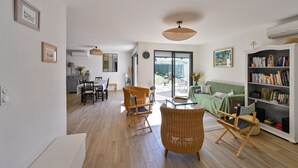 Un salón amplio con una mesa de comedor, sillas de mimbre, un sofá y una estantería.