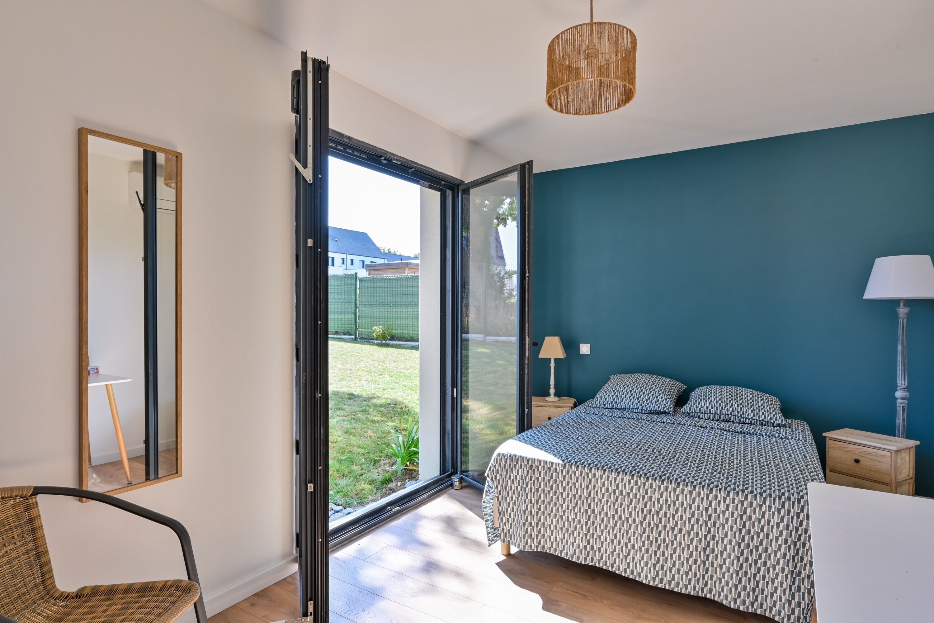 Ein Schlafzimmer mit einem Bett, einem Sessel, einem Nachttisch, einer Lampe und einem großen Fenster.