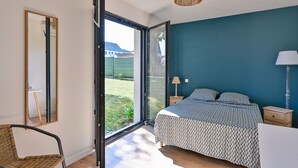 Un dormitorio con cama, una silla, mesita de noche, lámpara y un ventanal grande.
