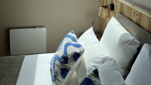 Een slaapkamer met dakraam, een bed met witte en blauwe kussens, een bedlamp en een radiator.