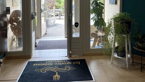 Een hotelentree met een houten vloer, een zwarte deurmat en zicht op het terras.