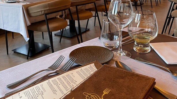 Een restaurant met gedekte tafels, menukaarten en een piano op de achtergrond.