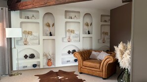 Een woonkamer met een bruine leren bank, een kussen van runderleer en decoratieve planken met planten en vazen.