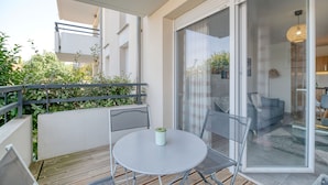 A modern balcony with a glass door leading to a living area, a round table with chairs, and a small plant on the table.