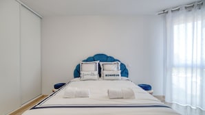 A neatly made bed with a blue headboard, two pillows with text, and two rolled towels.