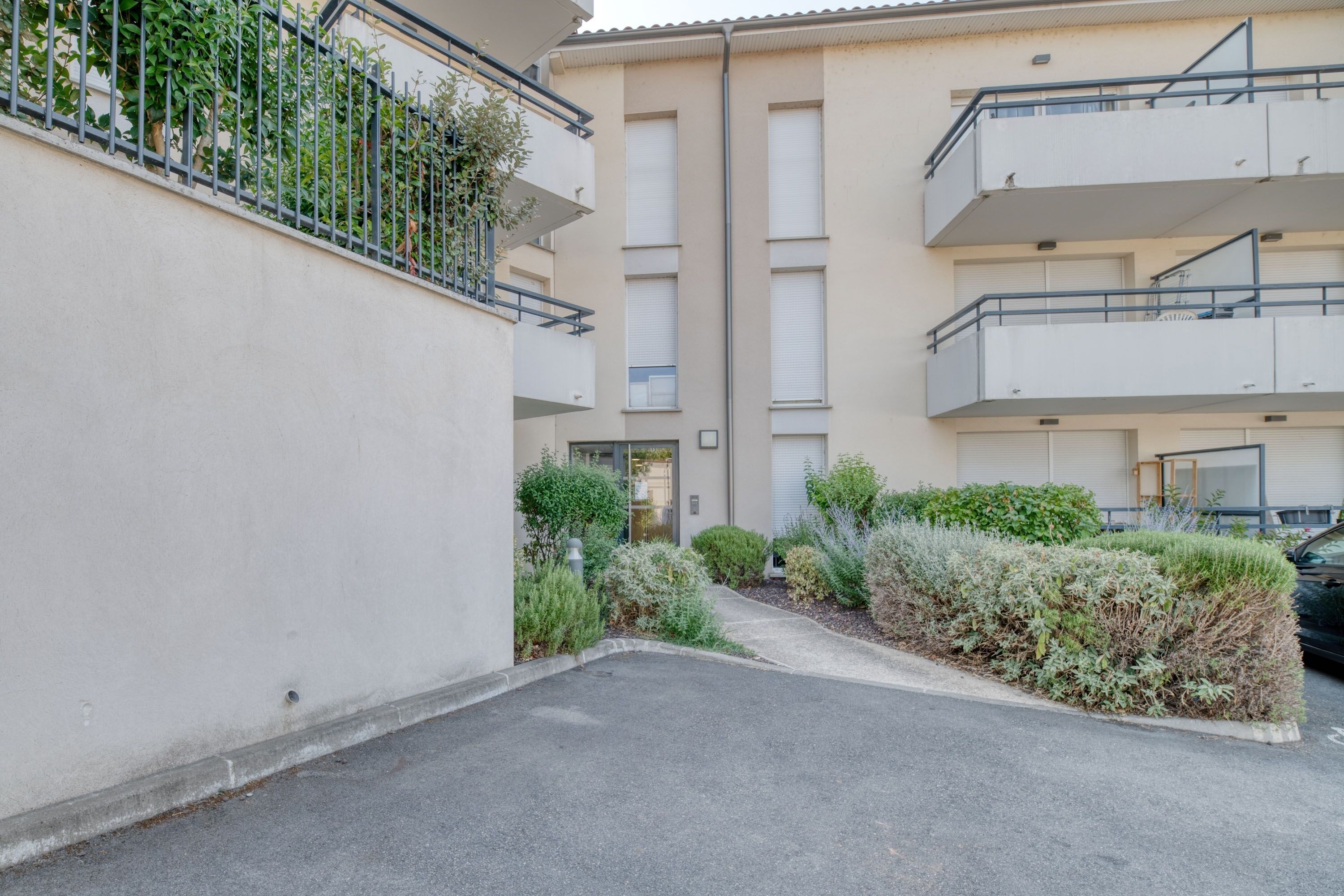 Un immeuble résidentiel à plusieurs étages, doté de balcons, d’un espace de stationnement et de parterres aménagés.