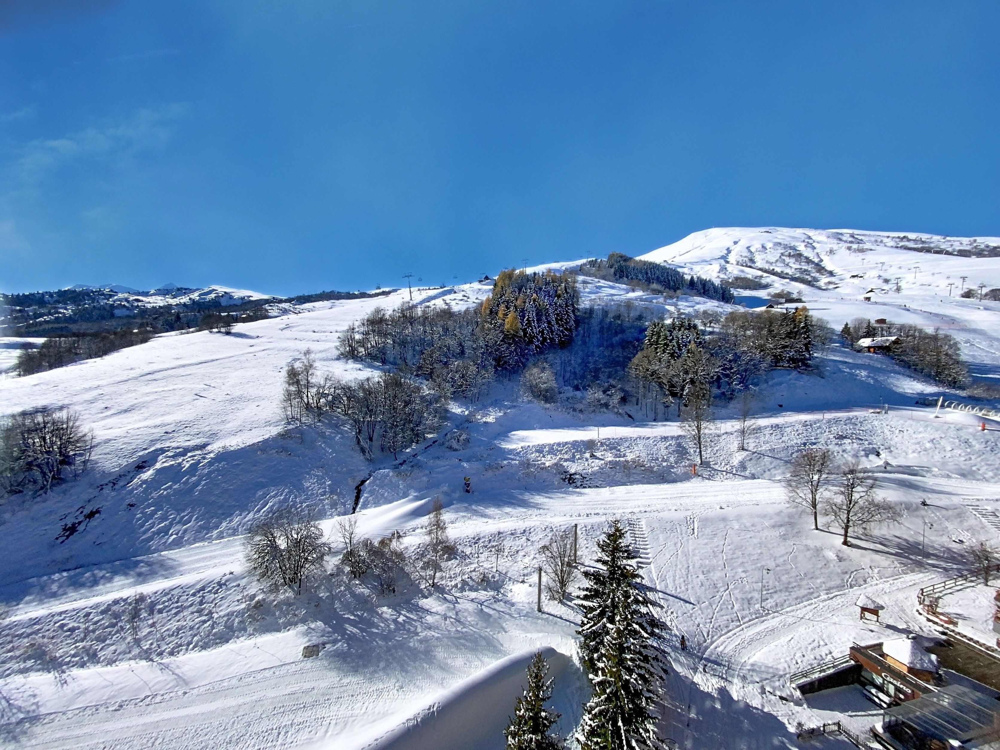 A snow-covered mountain landscape with ski slopes, trees, and a small building.