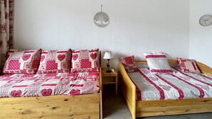 Une chambre avec deux lits en bois, chacun agrémenté de draps rouges et blancs, une petite table de chevet avec une lampe et une horloge murale.