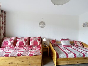 A room with two wooden beds, each with red and white bedding, a small bedside table with a lamp, and a wall clock. - Le Korrigan - Vue Montagne (Villarembert)