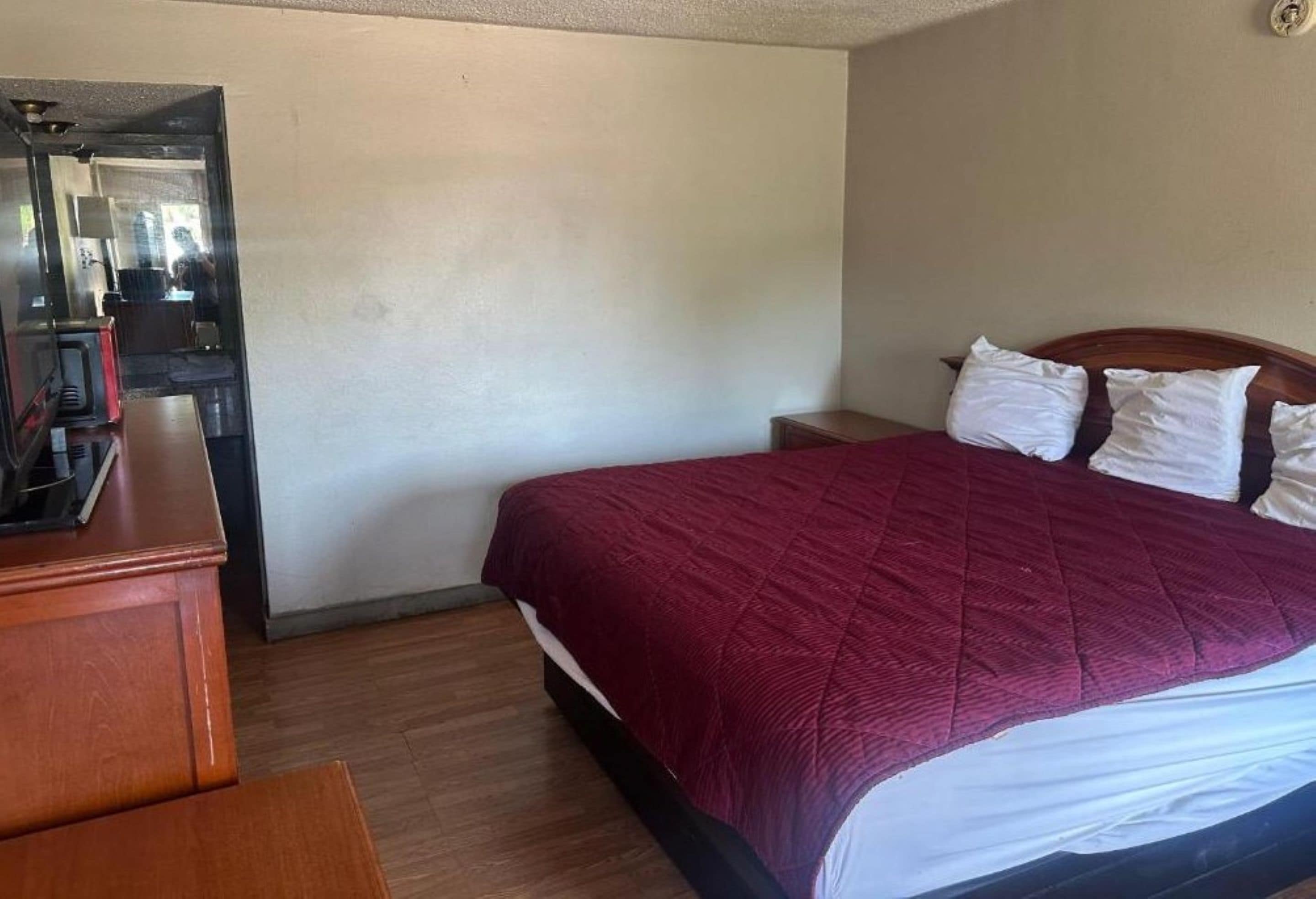 A hotel room with a bed, a wooden dresser, a nightstand, and a mirror.