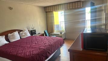 Een hotelkamer met een bed, een bureau, een stoel, een verwarming en een raam met gordijnen.