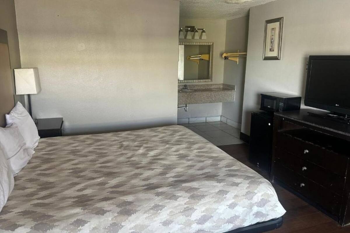 A hotel room with a large bed, a dresser, a television, and a bathroom visible in the background.